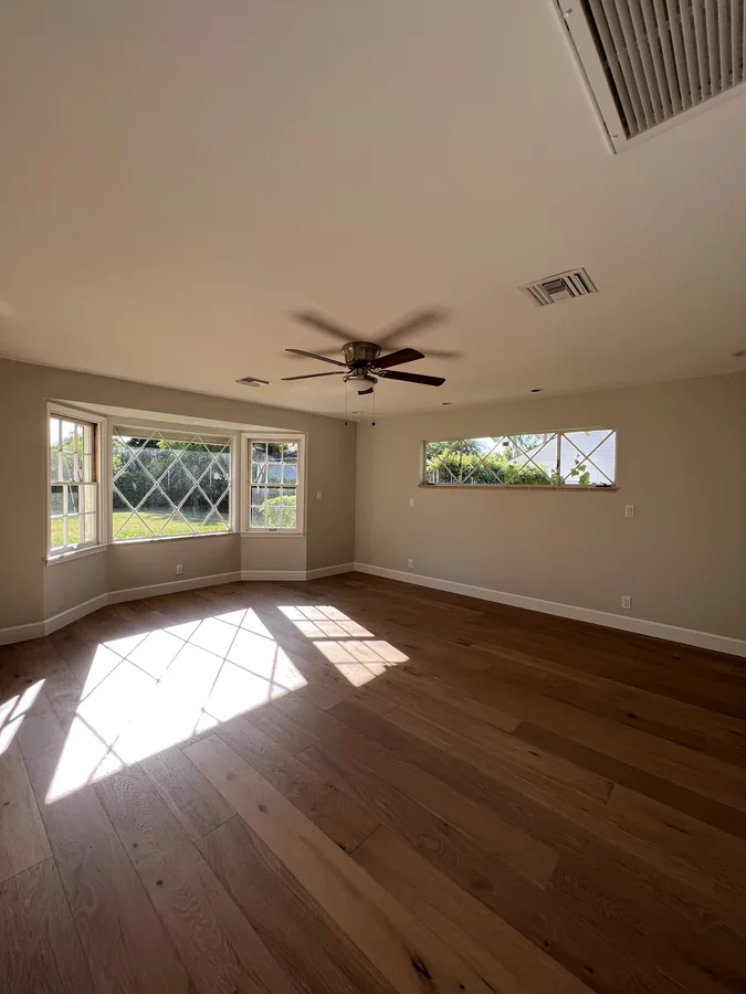Central Corridor Remodel: Renovated empty room with hardwood floors, ceiling fan and wide windows