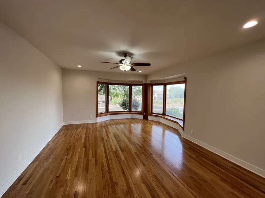 Home Renovation: Empty renovated room with hardwood flooring, ceiling fan and bay window